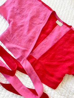 a pink shirt laying on top of a bed next to a red bag and white blanket