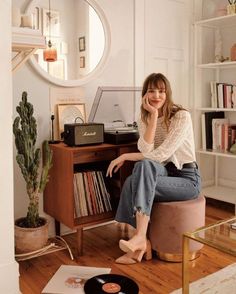 a woman sitting on top of a stool next to a record player and recordshelf