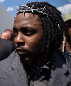 a man wearing a crown of silver crosses on top of his head with other men in the background