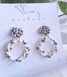 pair of white and purple flowered earrings on card next to green leafy plant