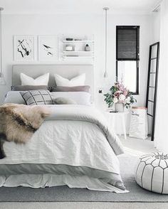 a bed with white sheets and blankets in a bedroom next to a window, some pictures on the wall