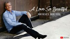 a man sitting on the ground next to a wooden wall with words above him that reads, a love so beautiful michael bollton