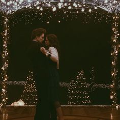 a man and woman dance in front of christmas lights