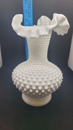 a white vase sitting on top of a table next to a measuring tape in front of it