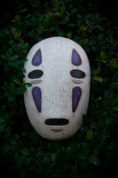 a white mask with purple eyes sitting in the bushes