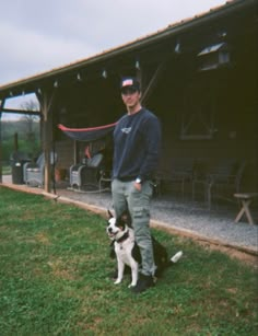 a man standing next to a black and white dog on top of a lush green field