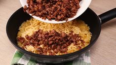 two spoons filled with chili and cheese in a skillet on top of a wooden table