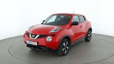 a red nissan juke is parked on a circular surface in front of a white wall