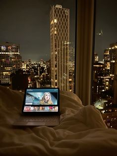 an open laptop computer sitting on top of a bed in front of a cityscape