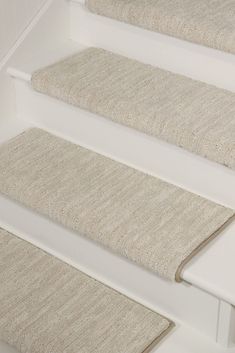 carpeted stair treads on the side of a white staircase with beige rugs