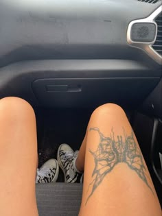 a person sitting in the passenger seat of a car with tattoos on their legs and feet