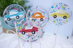 three lollipops with cars and sprinkles on them sitting on a table