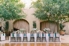 an outdoor wedding reception setup with white and blue linens, greenery and wooden chairs