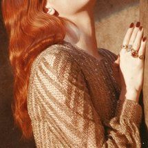 a woman with red hair leaning against a wall