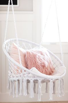 a white hammock hanging from the ceiling with pink pillows and tassels