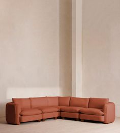 an orange leather sectional sofa sitting on top of a hard wood floor next to a white wall