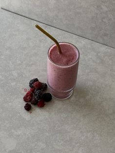 a pink smoothie with berries on the side and a straw sticking out of it