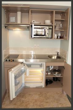 a small kitchen with an open refrigerator and microwave in the corner, next to a stove top oven