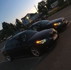 two cars parked side by side in a parking lot next to each other with their lights on