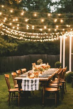 an outdoor dinner table with lights strung over it