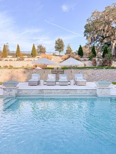 an empty pool with lounge chairs and umbrellas next to it in front of a stone wall