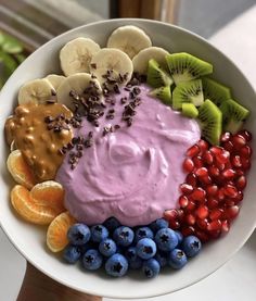 a white bowl filled with fruit and dip surrounded by kiwis, oranges, blueberries