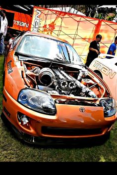 an orange sports car with its hood up and the engine in it's center