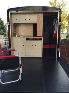 an empty chair sits in front of the back of a trailer that is being used as a kitchen