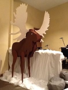 a large paper moose standing on top of a white table cloth covered floor next to a piano