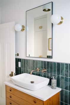 a white sink sitting under a bathroom mirror next to a wooden cabinet with two faucets