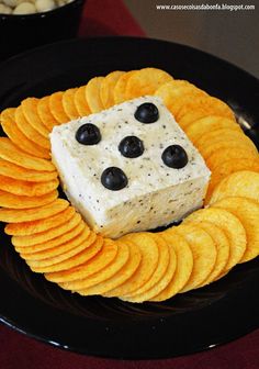 a black plate topped with crackers and a block of cheese covered in blueberries