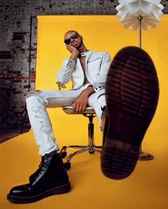 a man sitting on top of a chair next to a yellow wall with a pair of shoes