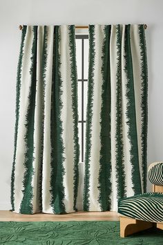 a green and white striped curtain hanging in front of a window next to a chair