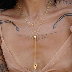 a woman with tattoos on her chest wearing a gold necklace and matching ring, holding onto the back of her neck