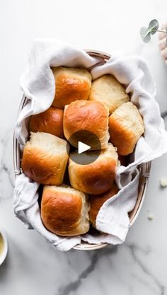 a basket filled with rolls on top of a white counter next to a cup of tea