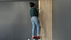 a person standing on a stepladder painting a wall with grey walls and wood slats