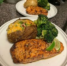 two white plates with baked potatoes, broccoli and salmon on them sitting on a counter