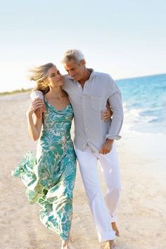 an older man and woman walking on the beach with their arms around each other as they hug