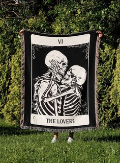 a woman holding up a blanket with a skeleton and roses on it in the grass