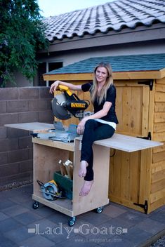 a woman sitting on top of a work bench with a saw in her hand and holding a mitt