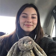 a woman is holding a stuffed animal in her lap and listening to headphones on