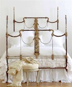 a bed with white linens and gold metal headboard, sitting on a hard wood floor