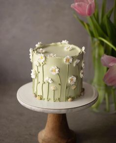 a green cake sitting on top of a white plate next to pink tulips