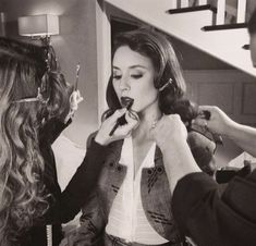 a woman getting her make - up done while another woman looks on in the mirror