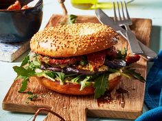 a sandwich with meat, lettuce and tomato on a cutting board next to a fork