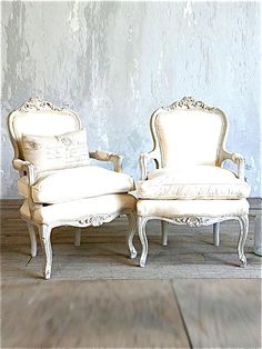 two white chairs sitting next to each other on top of a hard wood floor in front of a wall