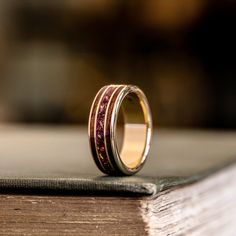 a wedding band with red and gold inlays sits on top of an open book