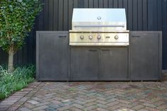 an outdoor bbq and grill in front of a black building with green plants on the side