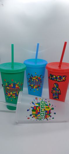 three different colored cups with straws in them on a white surface, one has a sticker and the other has a plastic lid