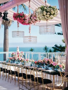 an outdoor dining area with flowers and chandeliers hanging from the ceiling, overlooking the ocean